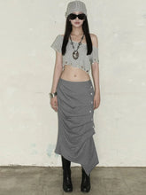 Person wearing a gray outfit with a skirt and crop top against a plain background